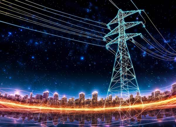 A tall, illuminated power transmission tower with high-voltage wires stretches towards a modern city skyline at dusk